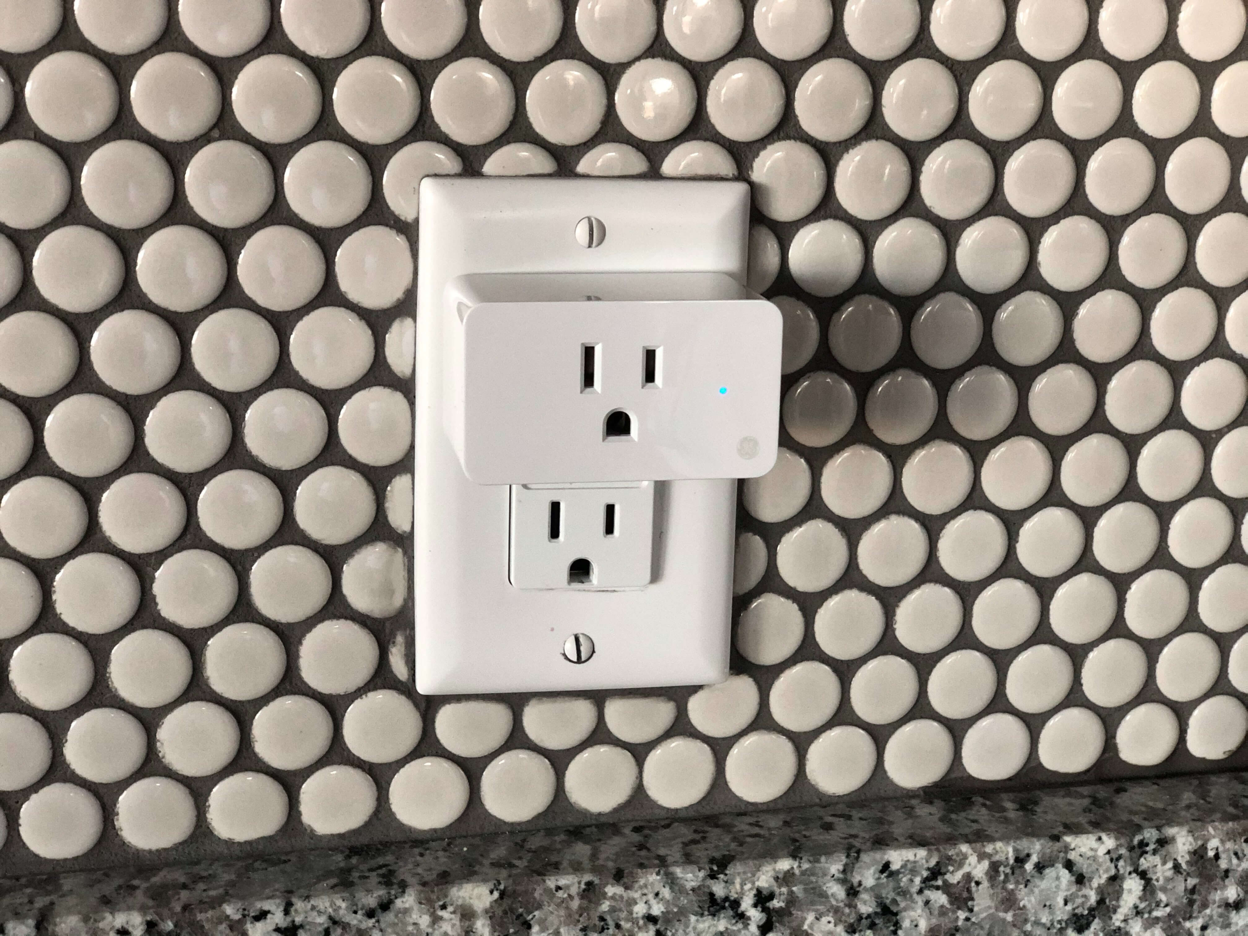 Smart plug connected to a wall outlet in a tiled kitchen backsplash.
