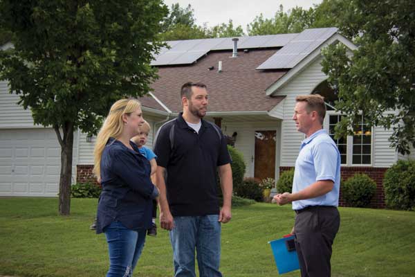 Young couple, members of Dakota Electric, stand outside their home after just installing rooftop solar panels.