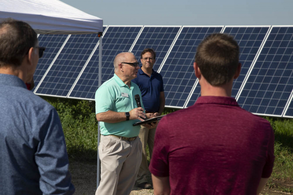 A man speaking to people with solar panels in the background.