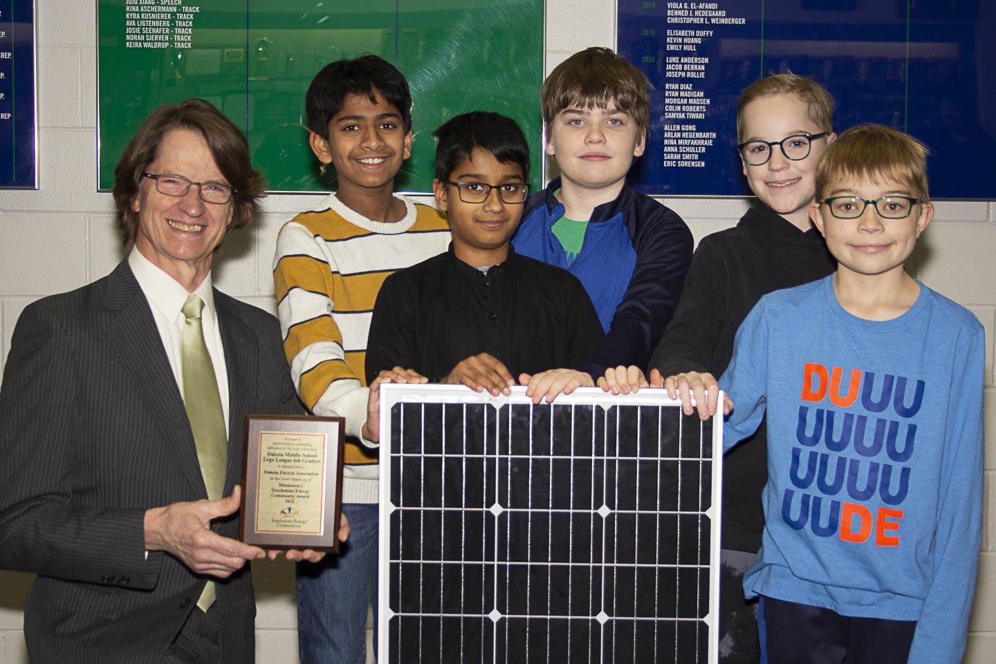 man posing with sixth grade boys and trophy and solar panel