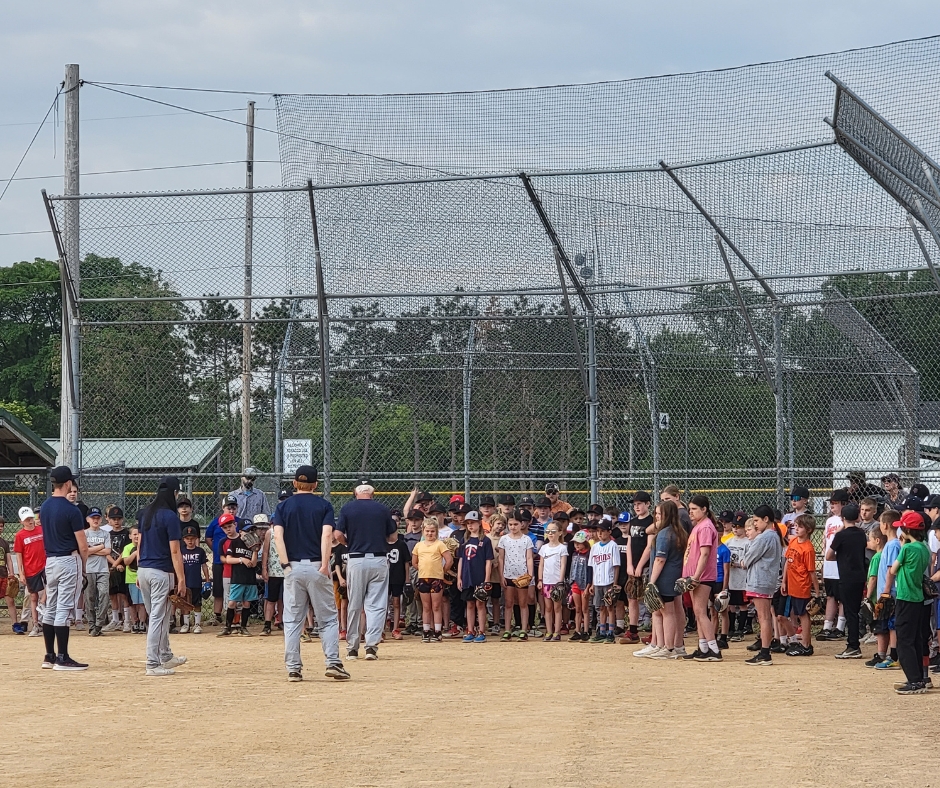 Baseball coaches teaching a crowd of young kids on a baseball diamond