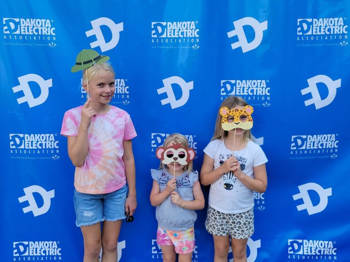 Three girls standing in front of a photo wall wearing silly masks.
