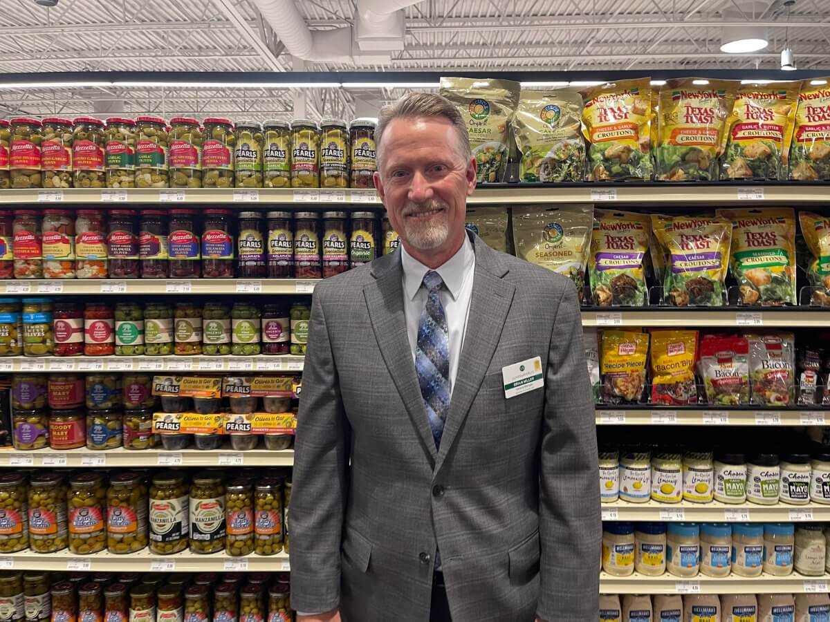 man in a suit in front of a grocery aisle of cereal