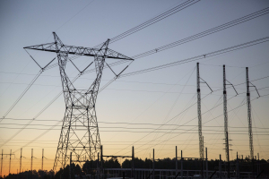 High-voltage transmission lines and towers silhouetted against a sunset sky at an electric substation.