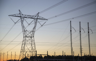 High-voltage transmission lines and towers silhouetted against a sunset sky at an electric substation.